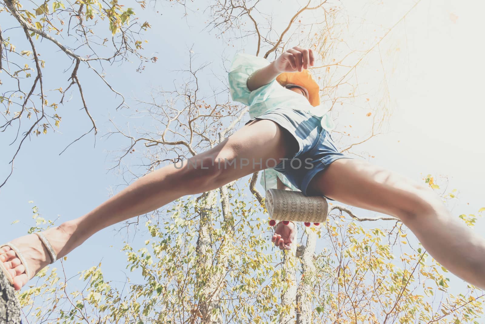 Low angle view of sexy woman short jeans midair by jumping, crossing step over camera shot below in forest with tree and sky overhead in concept travel, active lifestyle, overcome obstacles in life