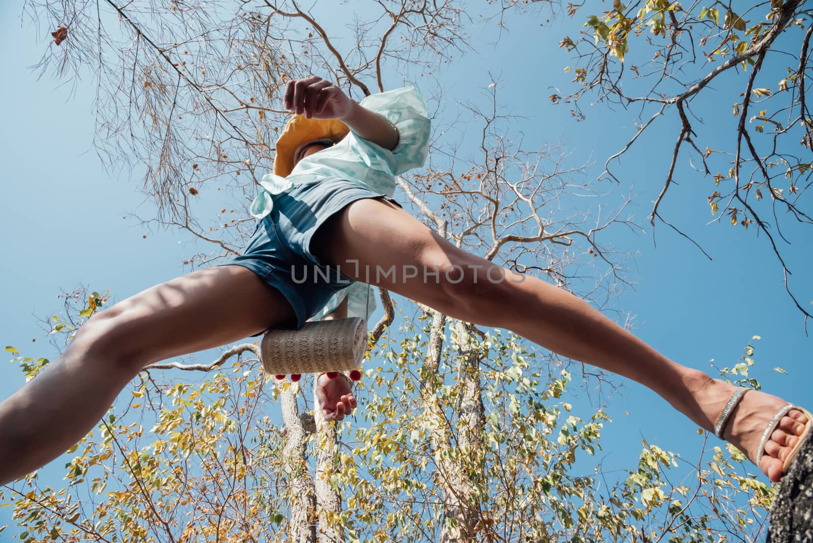 Low angle view of sexy woman short jeans midair by jumping, crossing step over camera shot below in forest with tree and sky overhead in concept travel, active lifestyle, overcome obstacles in life