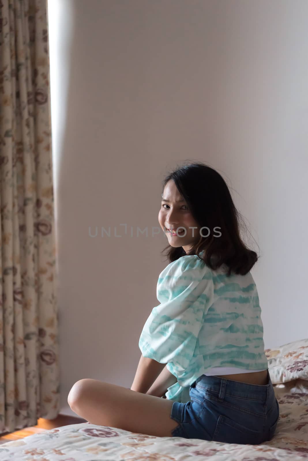 Asian pretty woman short jeans sitting on bed in bedroom alone with happiness and joyful emotion in concept cheerful feeling, pleasure, fun in life