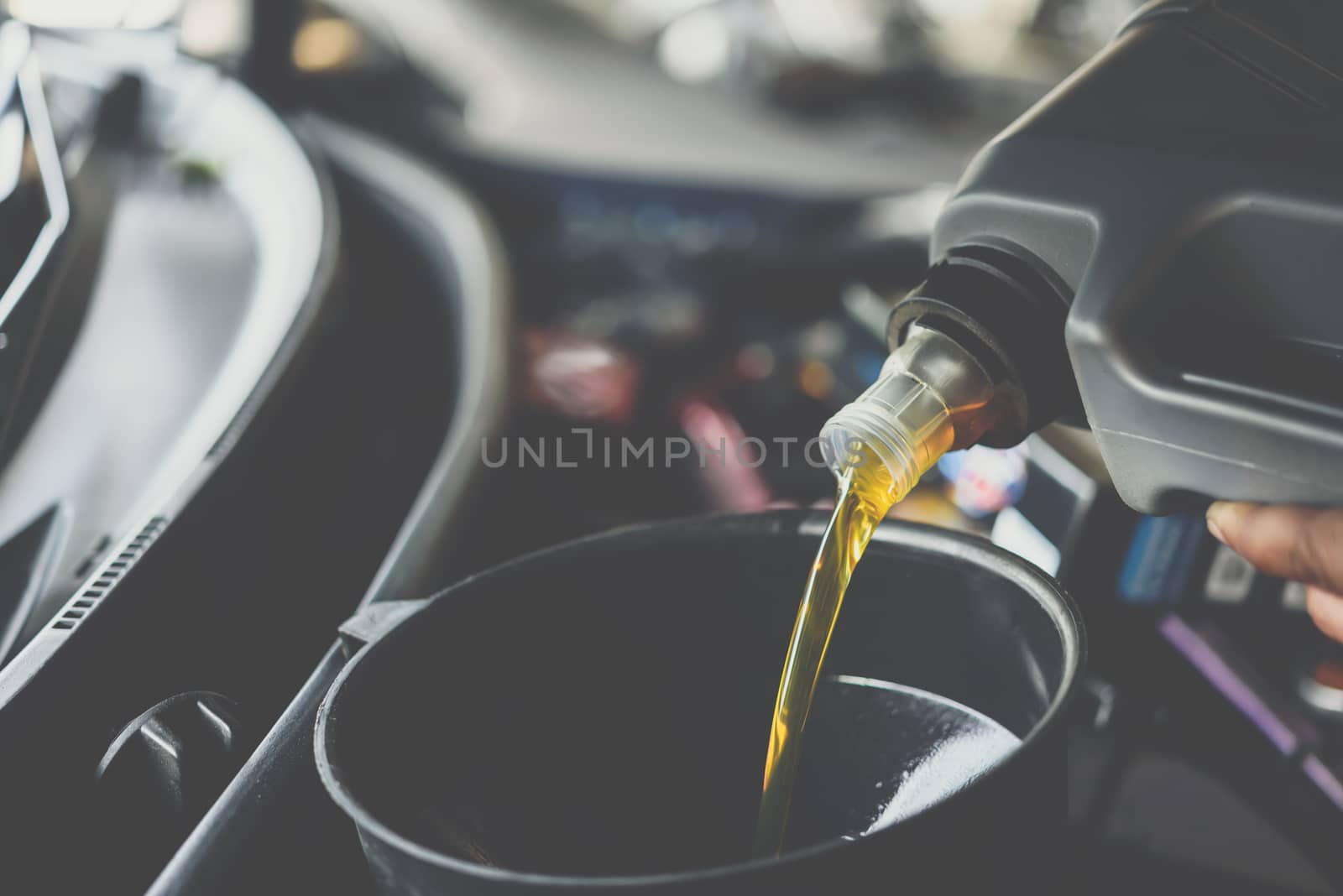 Car mechanic fills a fresh lubricant engine oil by PongMoji