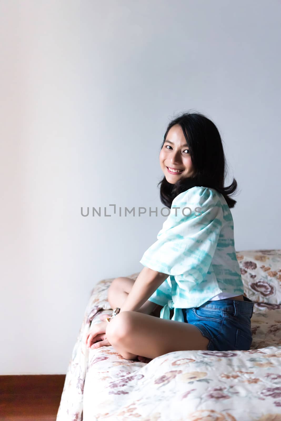 Asian pretty woman short jeans sitting on bed in bedroom alone with happiness and joyful emotion in concept cheerful feeling, pleasure, fun in life