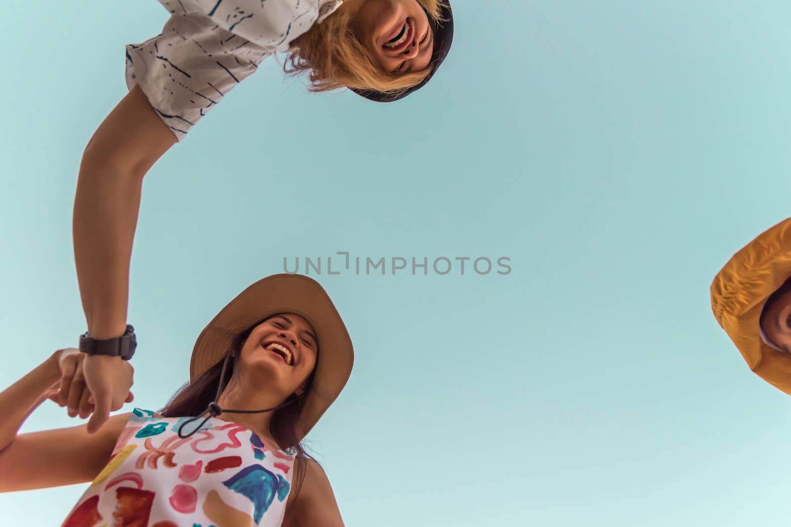 Low angle view of cute three asian women hold hands circle running round camera shot below with sky overhead in concept travel, happy and fun lifestyle, friendship. Pastel vintage style