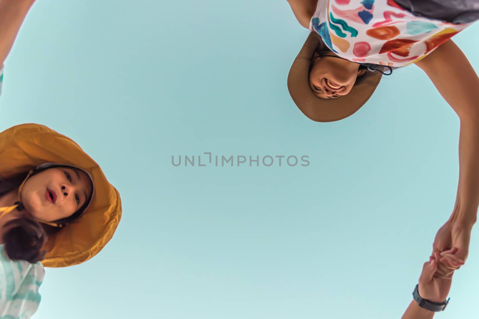 Low angle view of cute three asian women hold hands circle running round camera shot below with sky overhead in concept travel, happy and fun lifestyle, friendship. Pastel vintage style