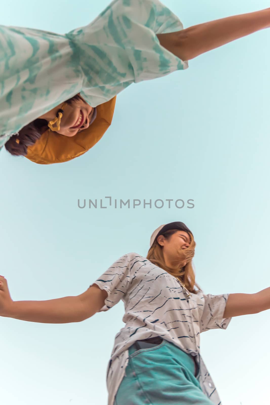 Low angle view of cute three asian women hold hands circle running round camera shot below with sky overhead in concept travel, happy and fun lifestyle, friendship. Pastel vintage style