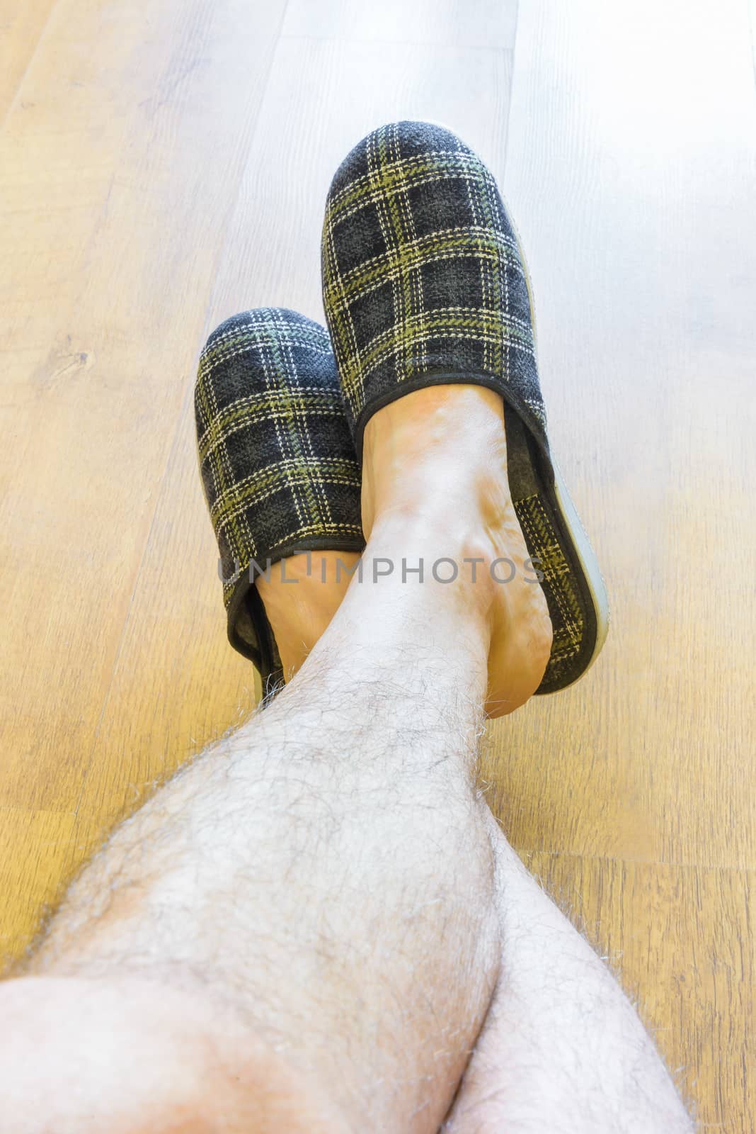 A man is relaxing while wearing warm slippers and showing hairy legs