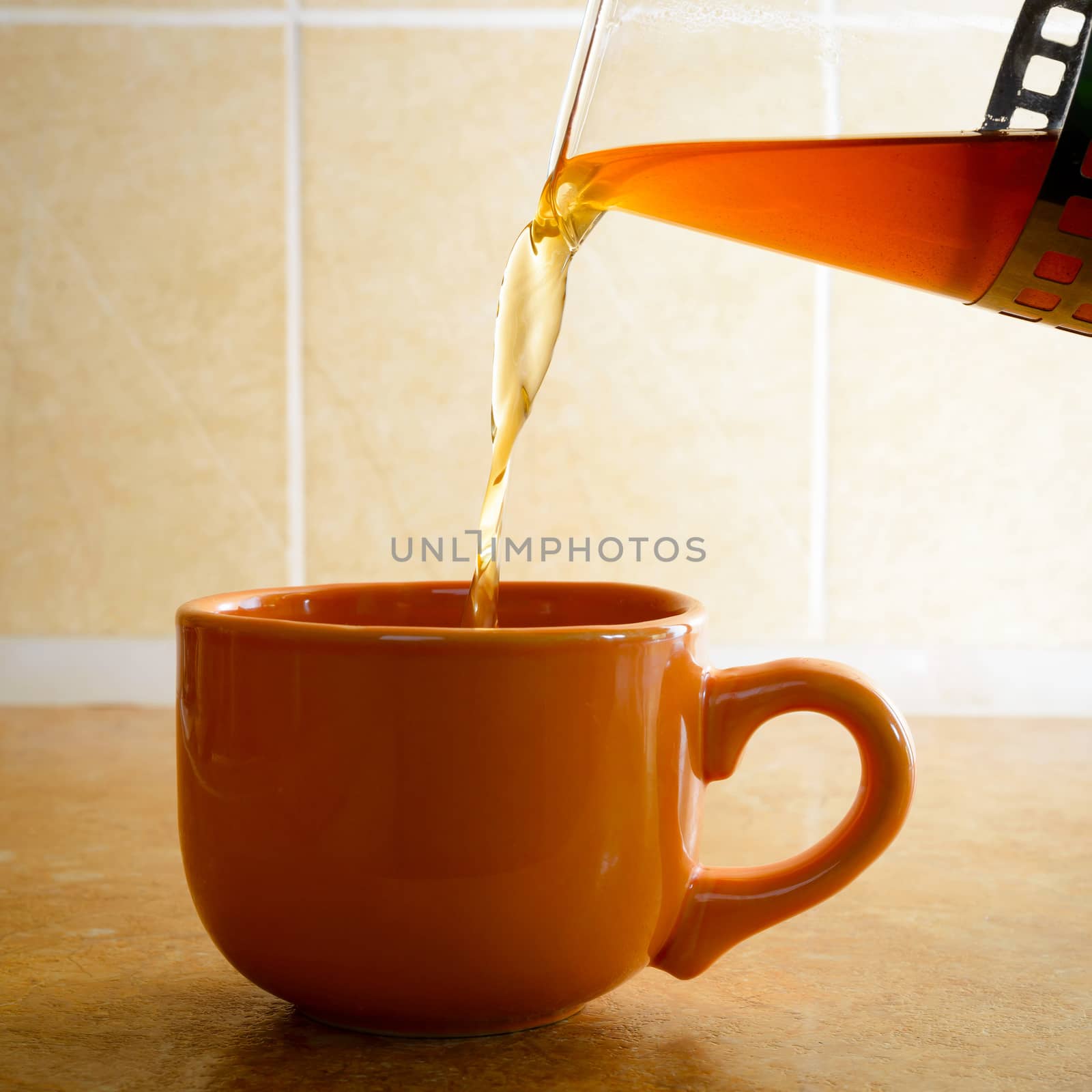 Pouring hot tea in an orange porcelain cup, in the kitchen