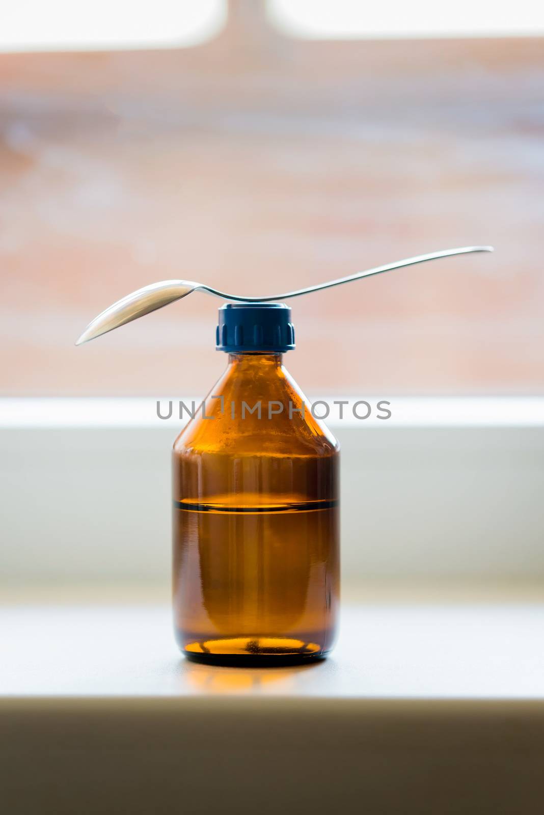 A cough syrup bottle with a spoon close to the window