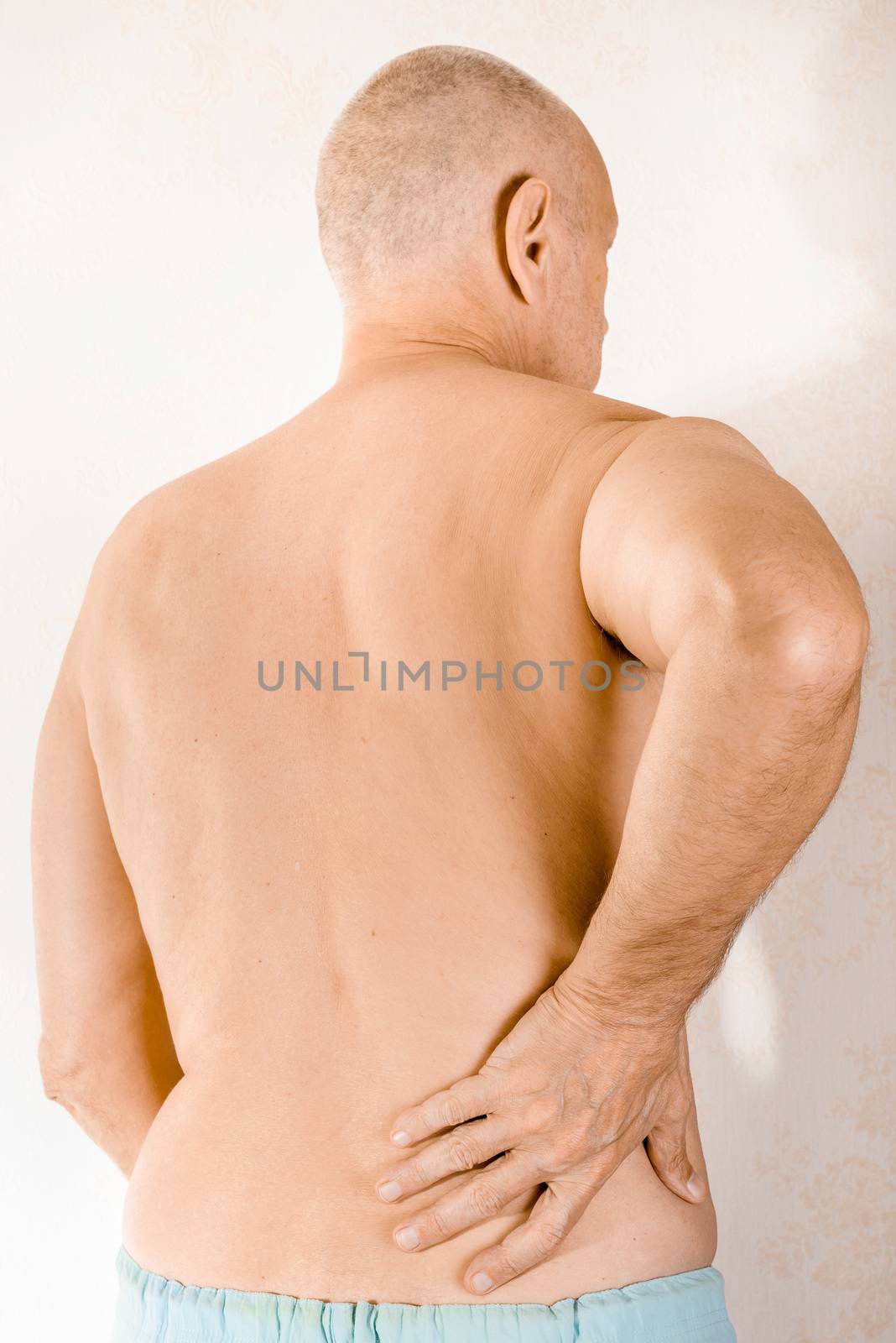 Man massaging the low back because of a painful lumbago due to a displacement of the lumbar vertebrae
