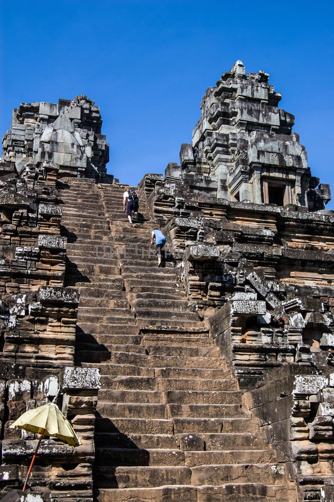 Two tourists Climbing the steep steps to the top of the ancient Khmer Hindu temple at Ta Keo, Angkor, Cambodia.  Built in 985 the steep stairway is designed so that pilgrims are prostrate before the gods.