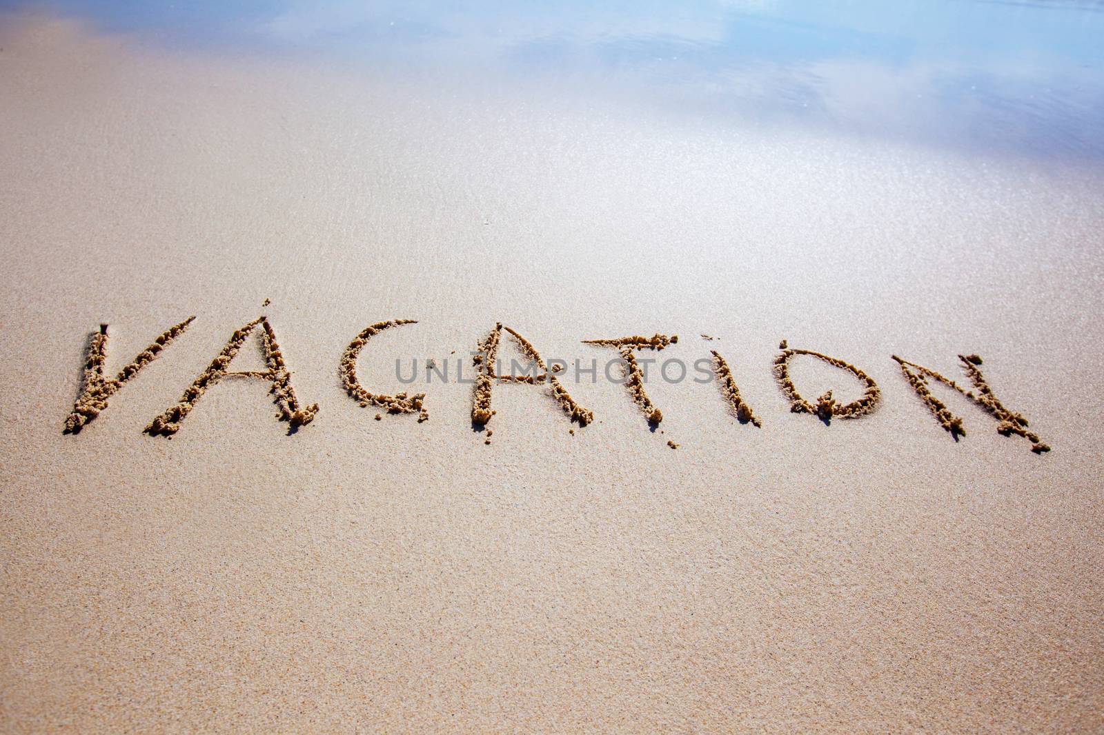 Word vacation written in a sandy tropical beach with soft sea wave