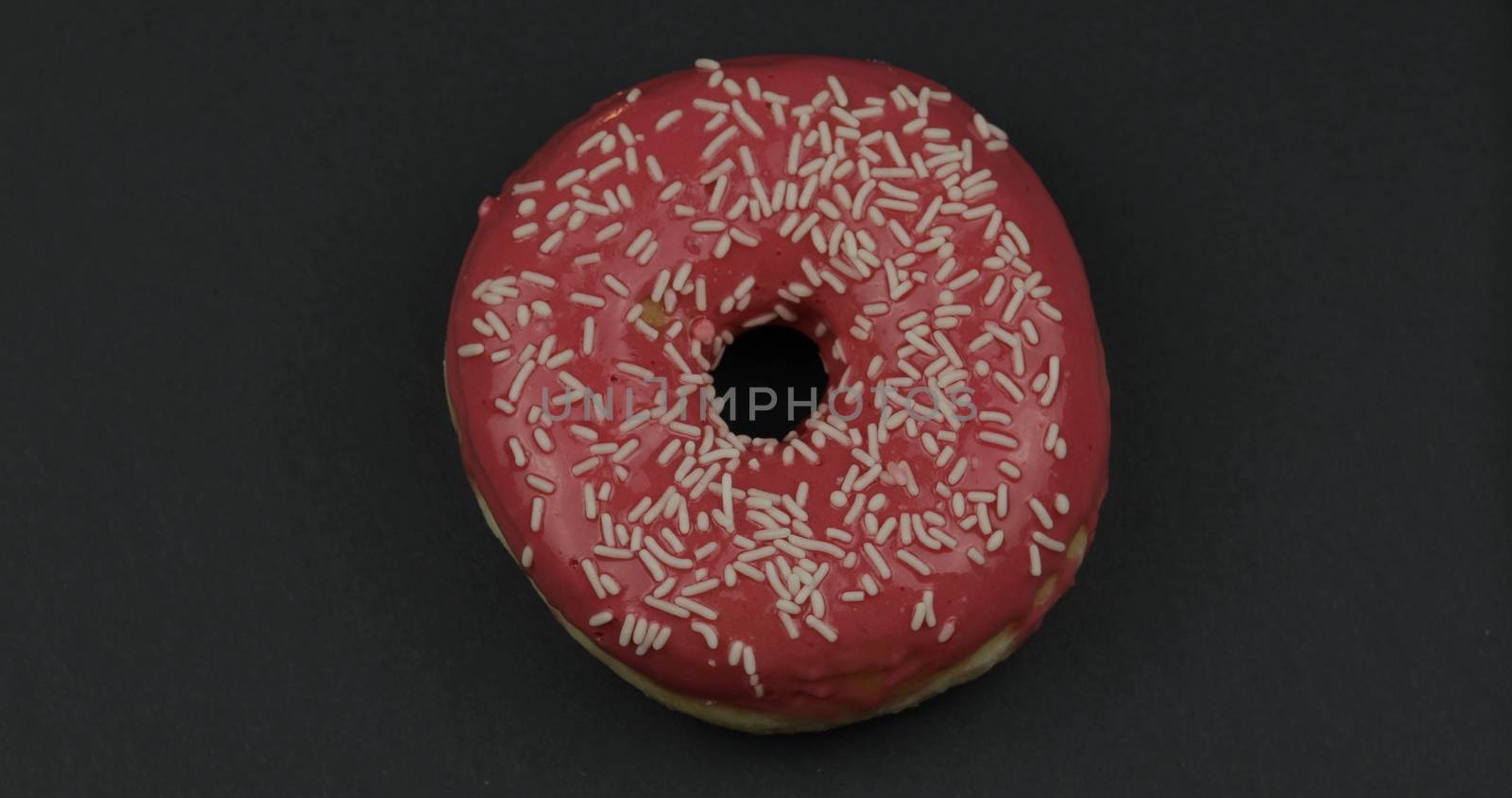 Delicious, tasty and fresh donut. Top view. Bright and colorful sprinkled sweet red donut close-up macro shot on a black background