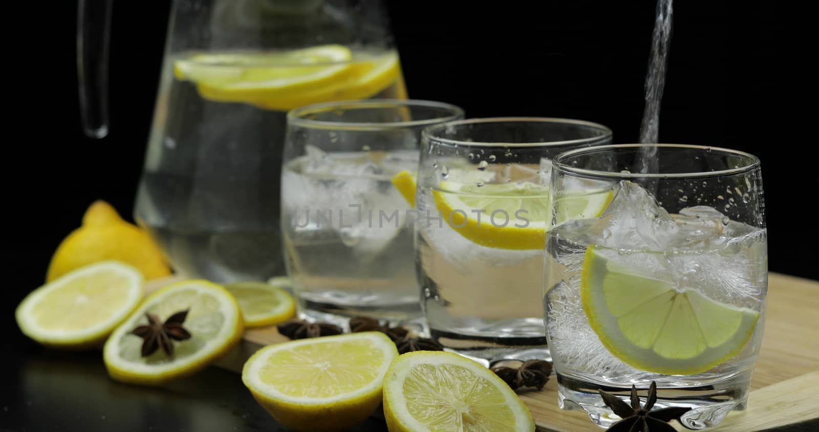 Pour lemon juice into glass with ice and lemon slices. Lemon cocktail with ice on dark background. Refreshing alcoholic cocktail drink