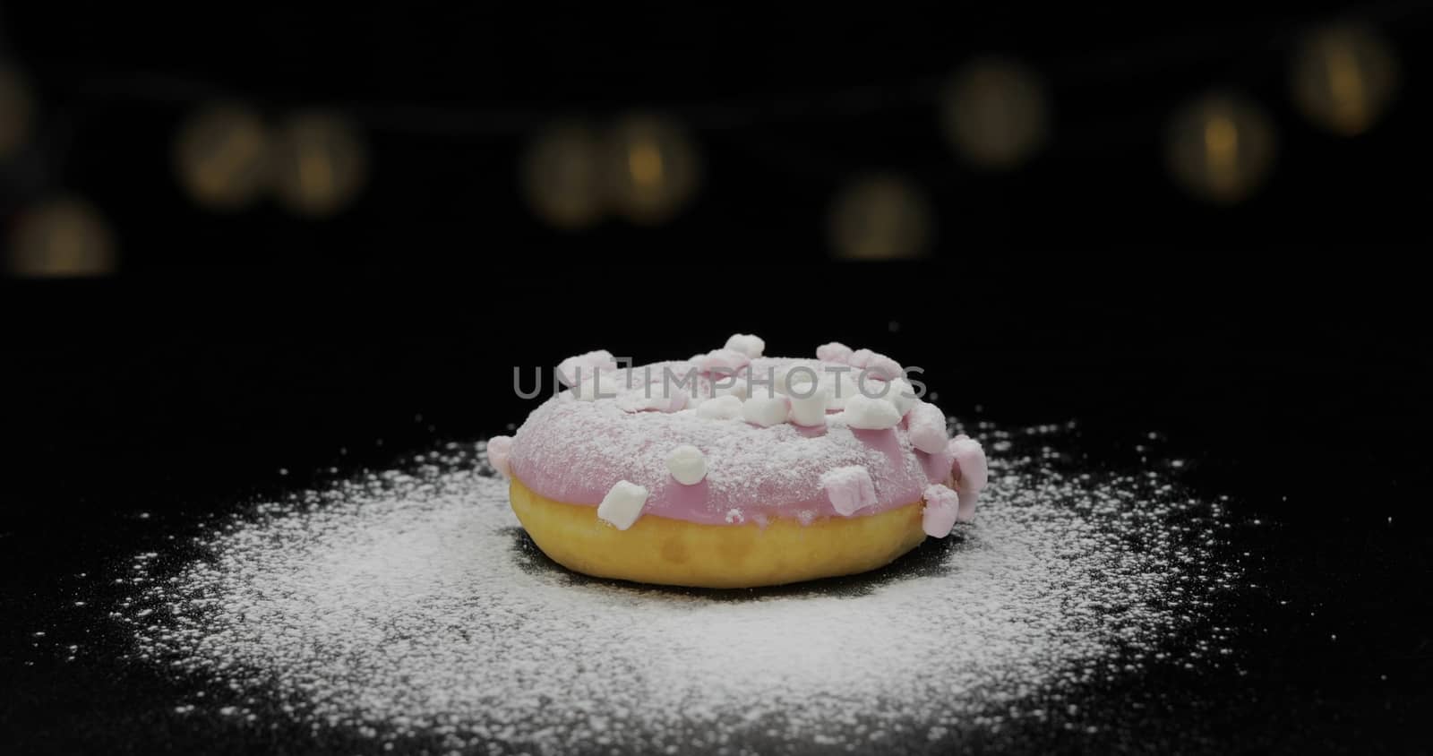 Tasty fresh pink donut lay on the black surface with icing sugar powder