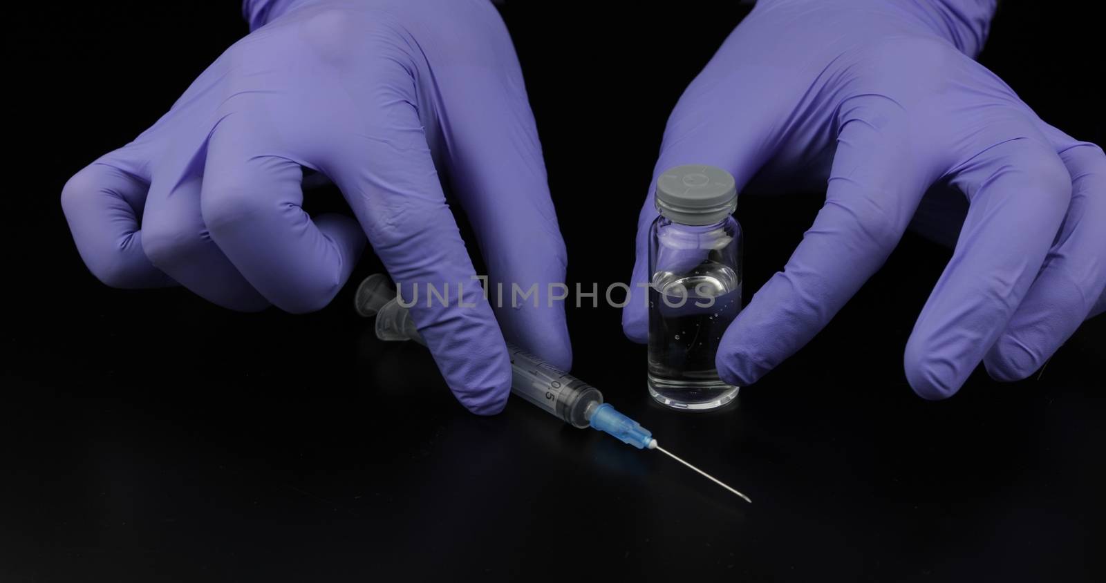 Doctor's hands with syringe, ampoule with vaccination on black background.