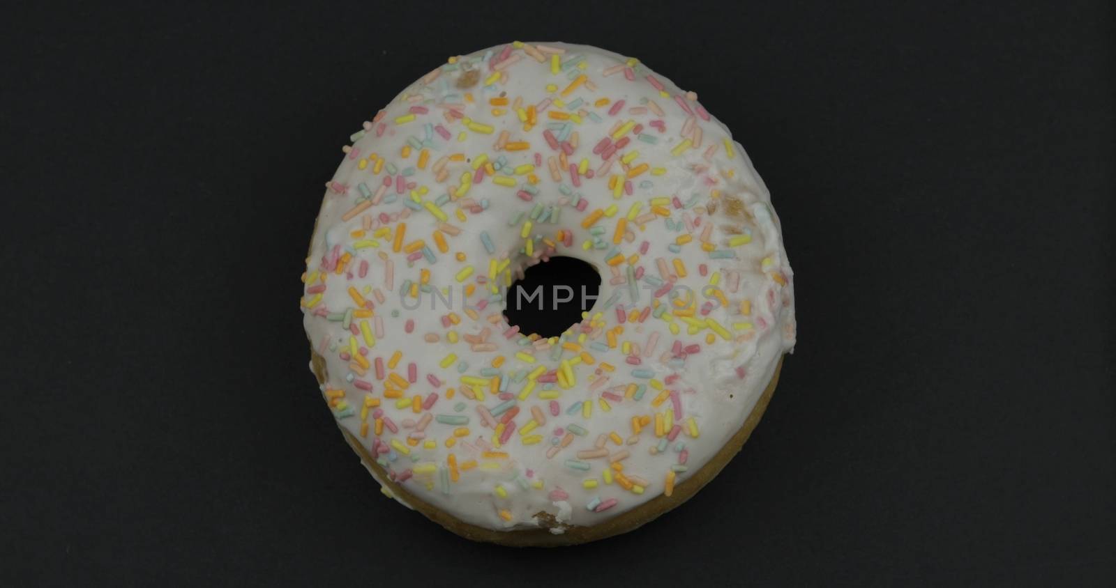 Delicious, tasty and fresh donut. Top view. Bright and colorful sprinkled sweet white donut close-up macro shot on a black background