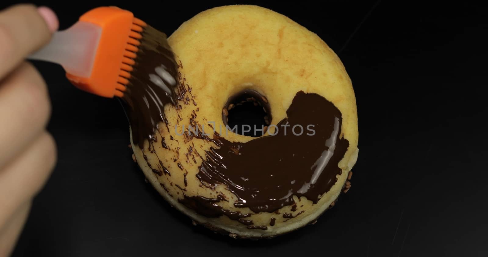 Delicious melted chocolate syrup spreading over a donut on black background. Melted dark chocolate flows on the doughnut