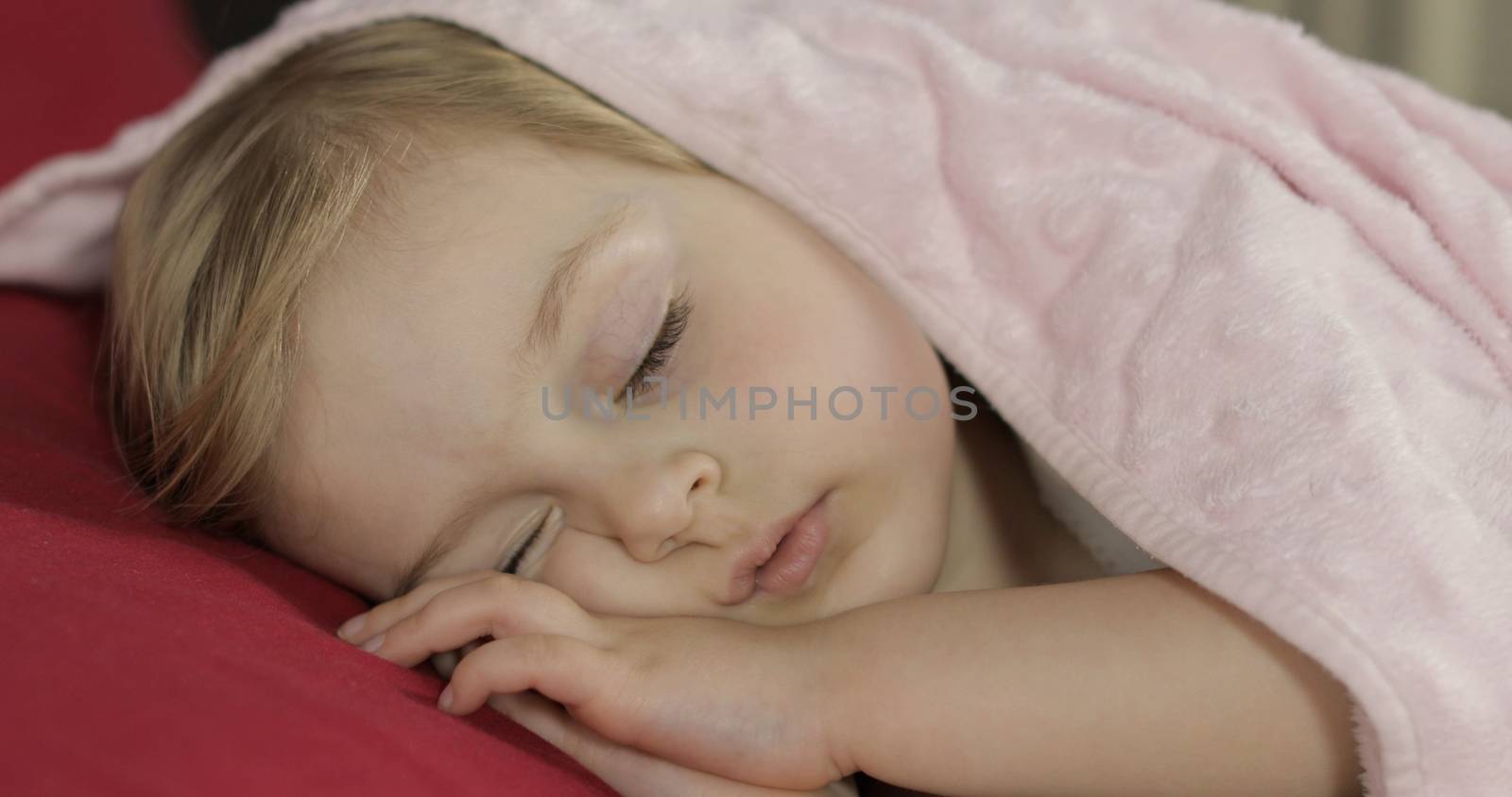 Cute baby girl sleeping on cozy bed at home. Pretty, little girl sleeping in morning light. Close-up portrait of child naps. Concept of peaceful sweet dreams