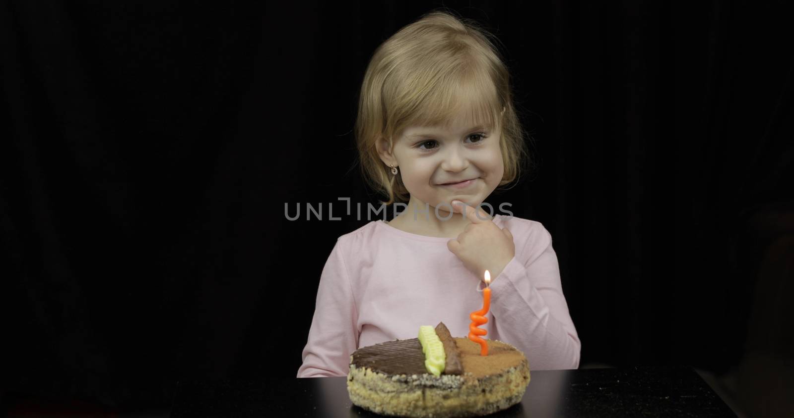 Little cute girl making a wish before blow out festive candle on birthday cake. Happy 4 years child. Sweet, cute blonde hair girl