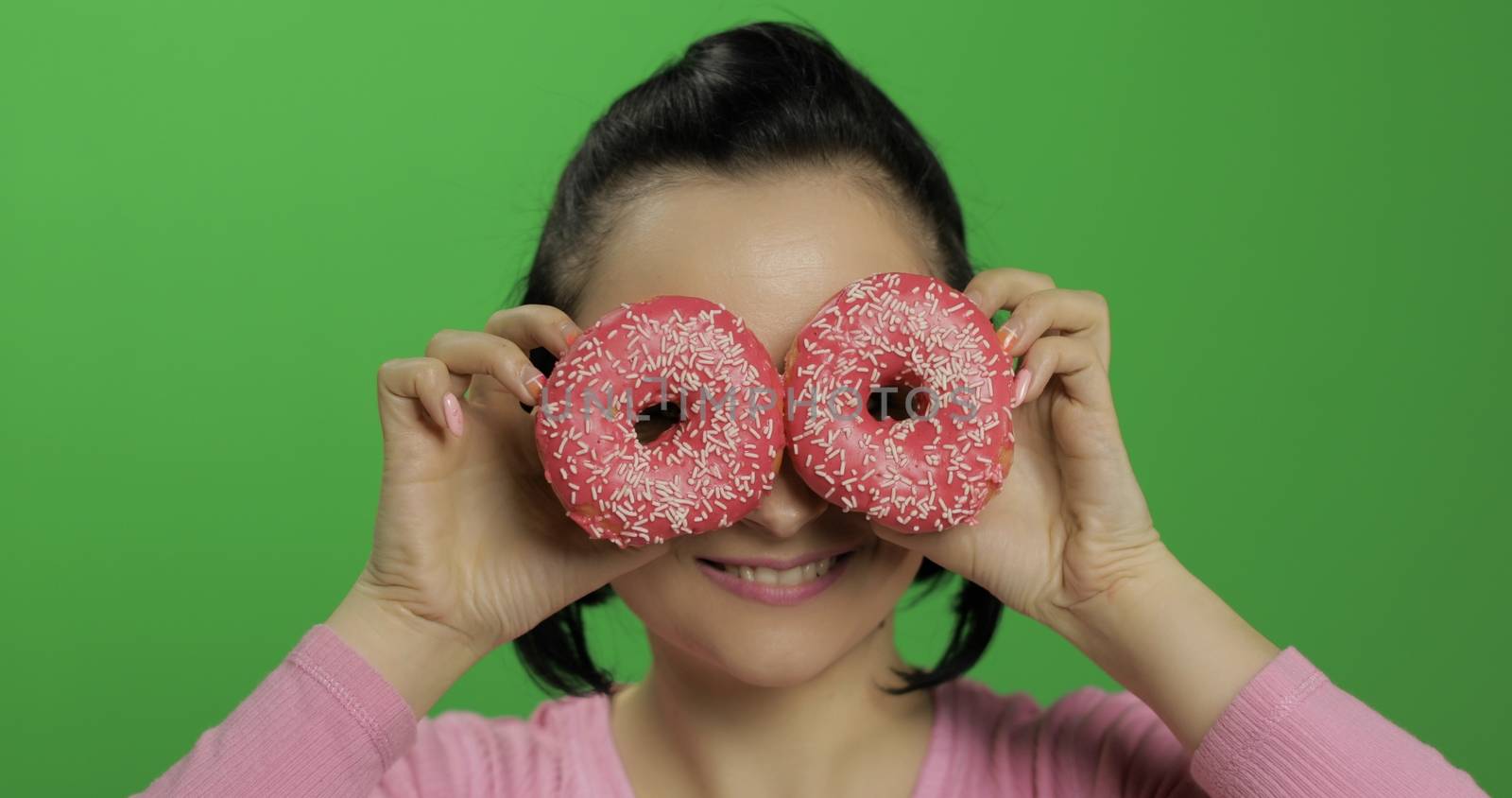 Happy beautiful young girl on a chroma key background having fun with donuts. Cute woman in a pink shirt posing with donuts. Making faces