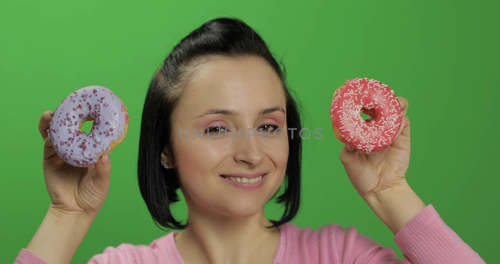 Happy beautiful young girl on a chroma key background having fun with donuts. Cute woman in a pink shirt posing with donuts. Making faces