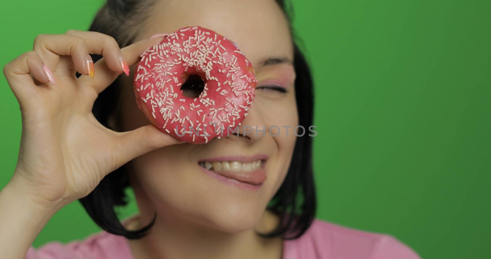 Happy beautiful young girl on a chroma key background having fun with donuts. Cute woman in a pink shirt posing with donuts. Making faces