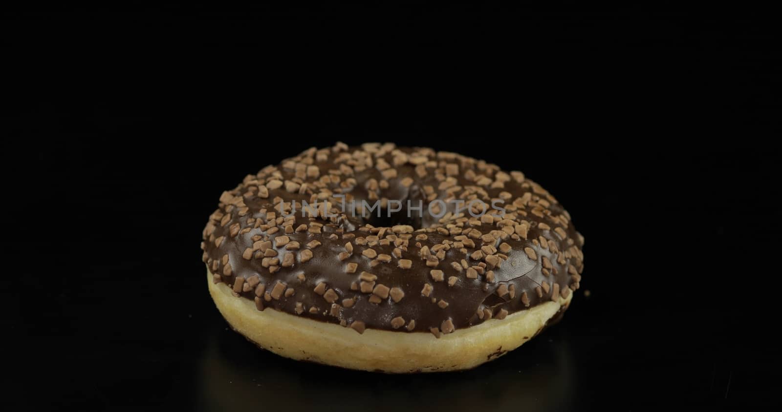 Delicious, tasty and fresh donut. Bright and colorful sprinkled sweet brown donut close-up macro shot on a black background