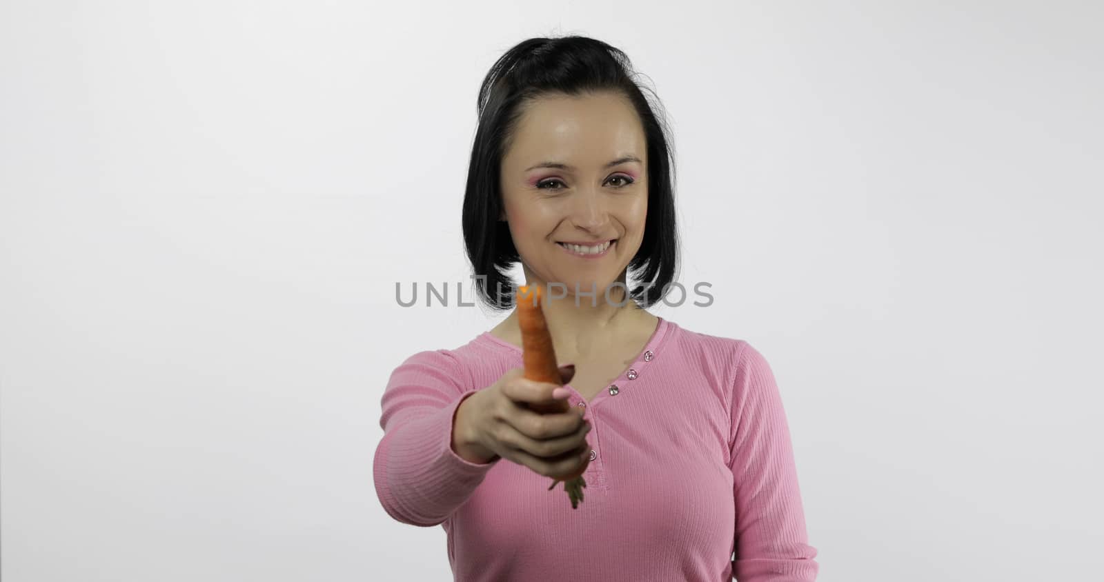 Young beautiful woman with big carrot. Offer bite to viewer. Healthy nutrition. Model eating vegetables