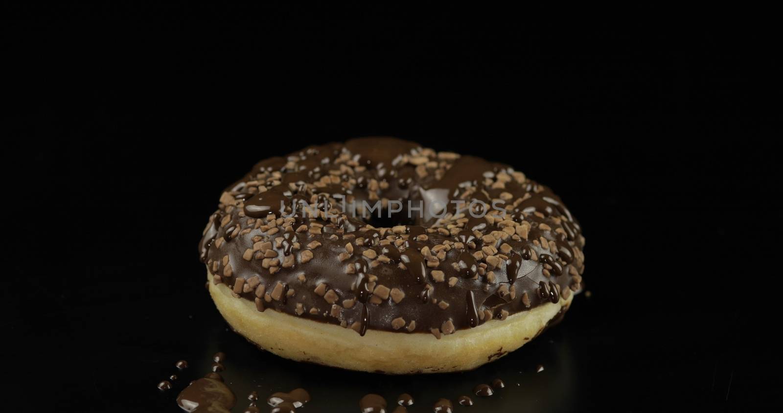 Delicious, tasty and fresh donut with melted dark chocolate. Bright and colorful sprinkled sweet brown donut close-up macro shot on a black background