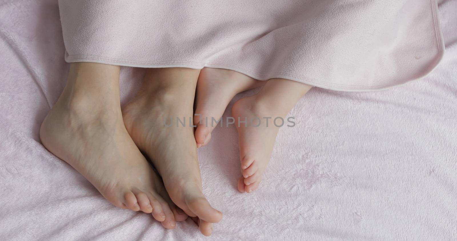 Two pairs of legs of the happy family in bed under the coverlet - mother and daughter. Sleeping of the baby and his mom on the bed in the morning. Happy family peaceful sweet dreams concept