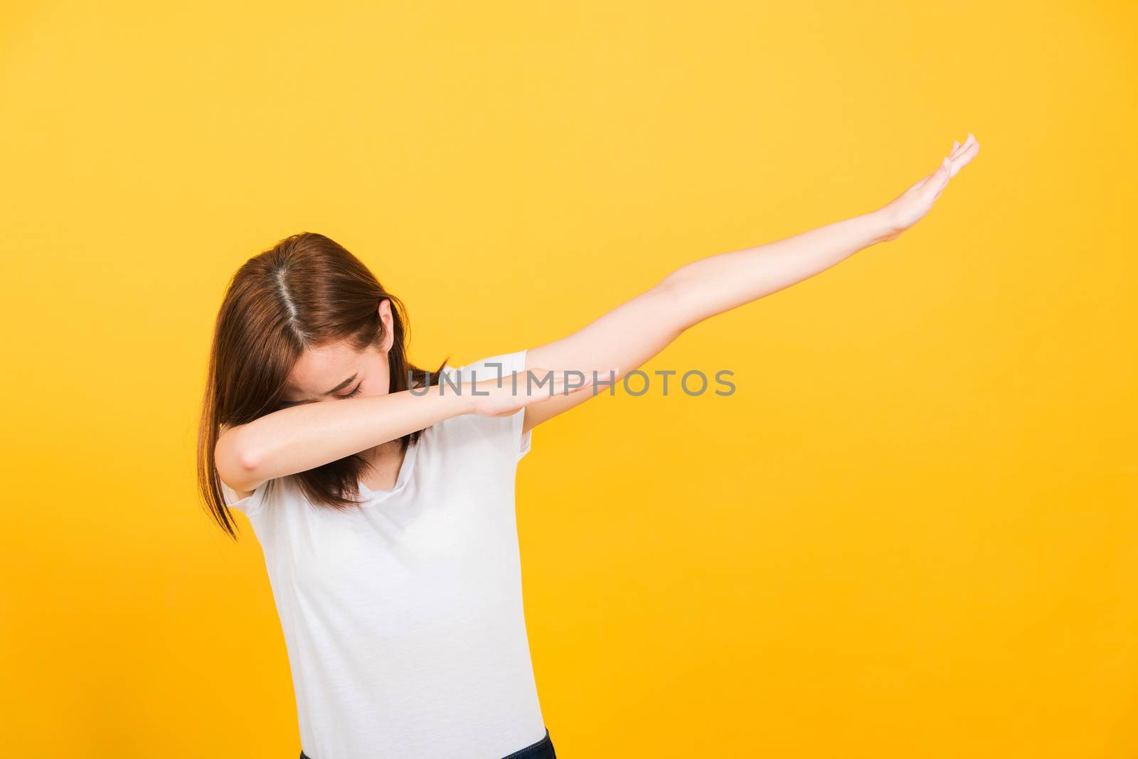 Asian happy portrait beautiful cute young woman teen smile standing wear t-shirt move showing DAB dance against gesture isolated, studio shot on yellow background with copy space