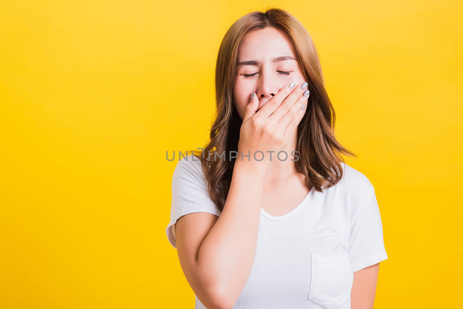 Portrait Asian Thai beautiful young woman emotions tired and sleepy her yawning close mouth open by hand, shoot a photo in the studio on yellow background, There was copy space, insomnia concept