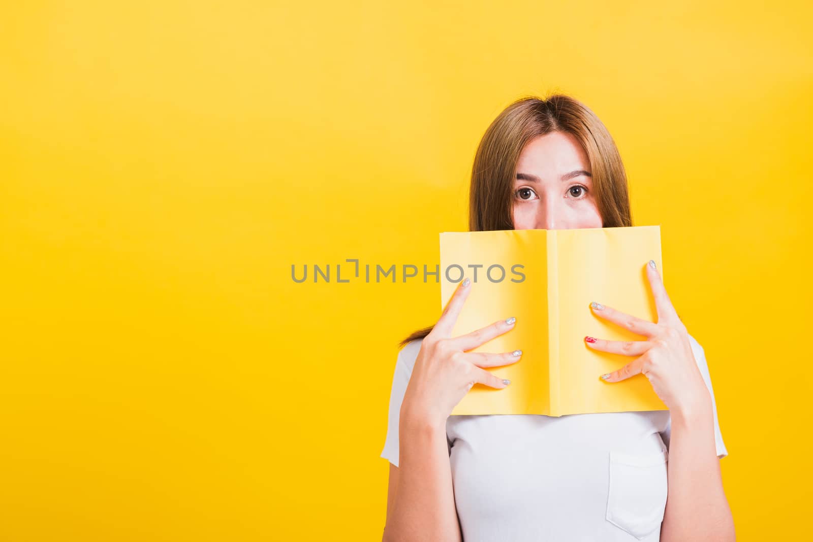 Portrait Asian Thai beautiful happy young lifestyle woman stands holding yellow book or diary her looking to camera, studio shot isolated on yellow background, with copy space