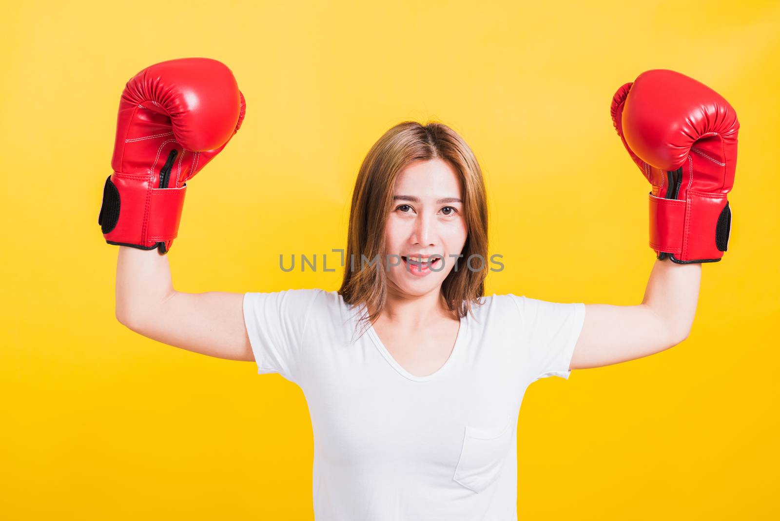 Portrait Asian Thai beautiful young woman standing smile raise hand showing hands during wearing red boxing gloves, studio shot isolated on yellow background, There was copy space for text