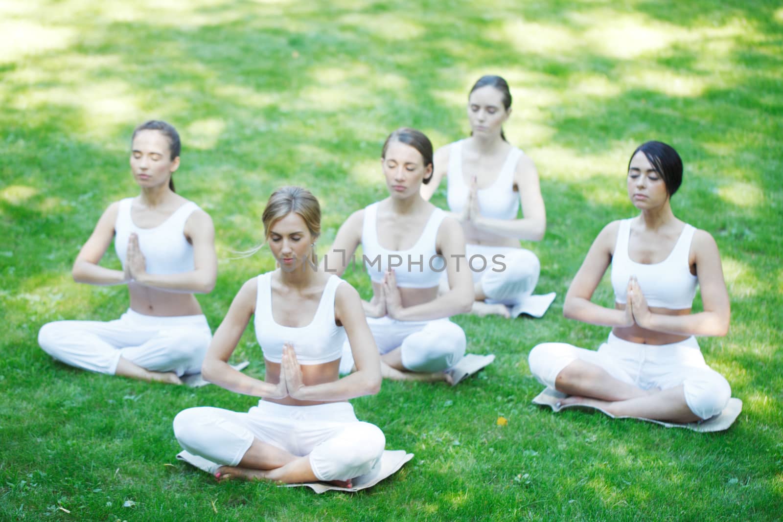 Women in white sportswear sitting in lotus position during group yoga training class at park