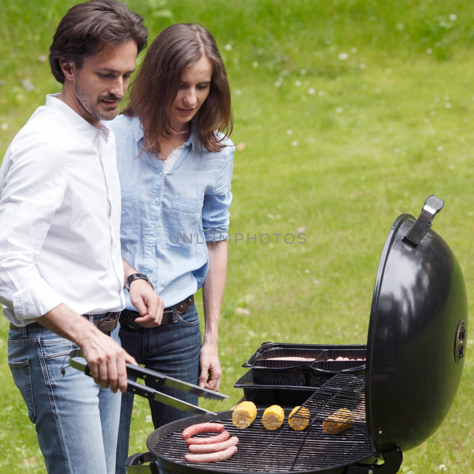 Couple cooking food corn vegetables sausage on barbecue grill at backyard