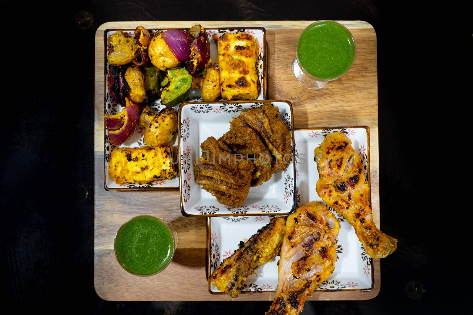 shot of delicious chicken drum sticks legs, lollypop, mutton patties, cottage cheese, mint chutney in glasses for a punjabi north indian barbeque meal. A perfect mix of meat and vegetarian elements in mughal style