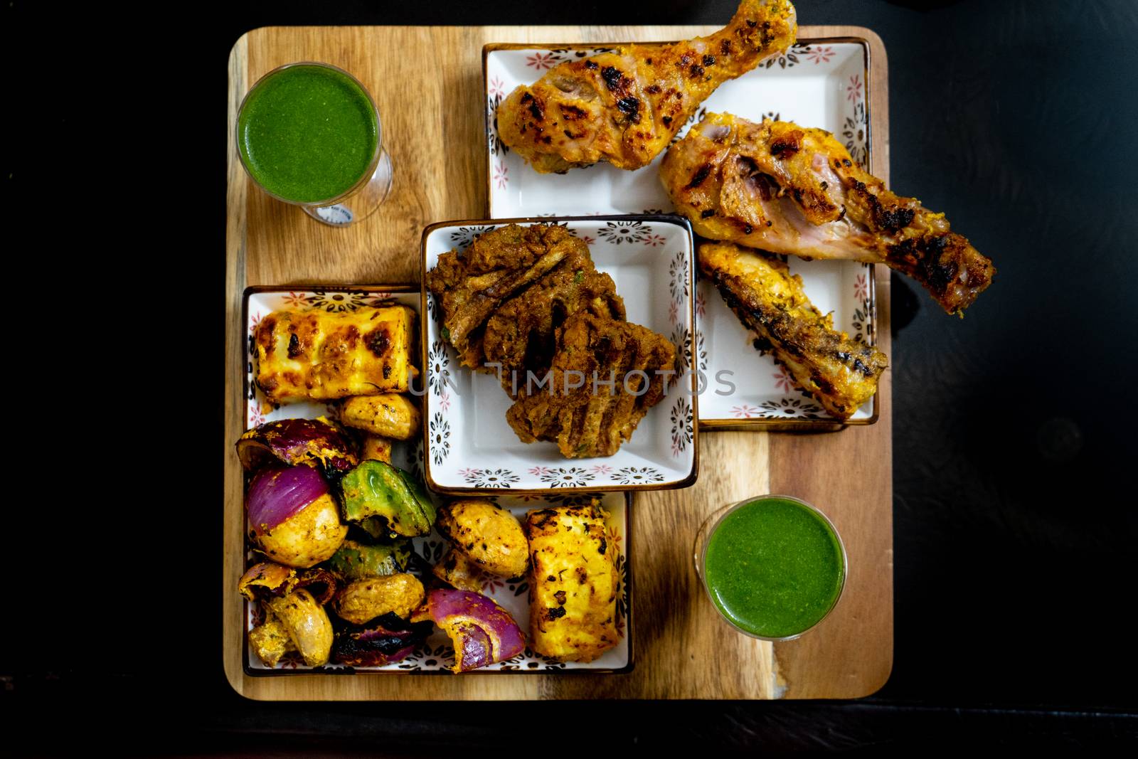 shot of delicious chicken drum sticks legs, lollypop, mutton patties, cottage cheese, mint chutney in glasses for a punjabi north indian barbeque meal. A perfect mix of meat and vegetarian elements in mughal style
