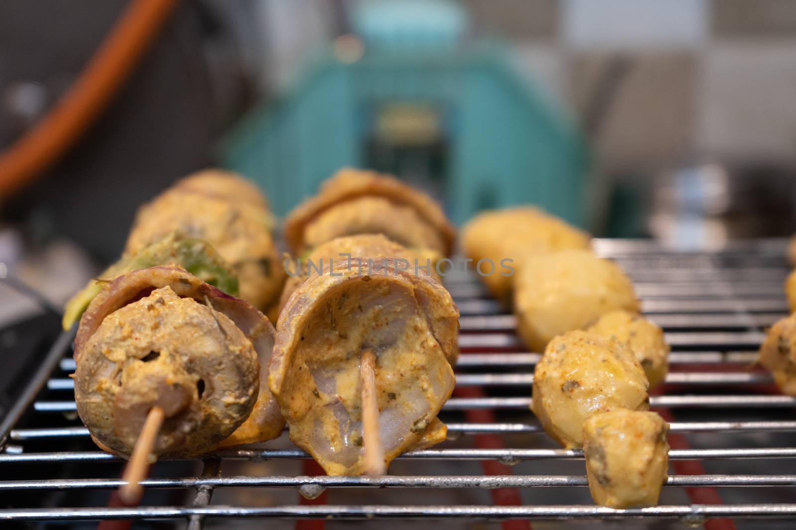 Wooden skewer with vegetables like mushroom, chilli pepper, green pepper onions and potatoes cooking on an electric grill by Shalinimathur