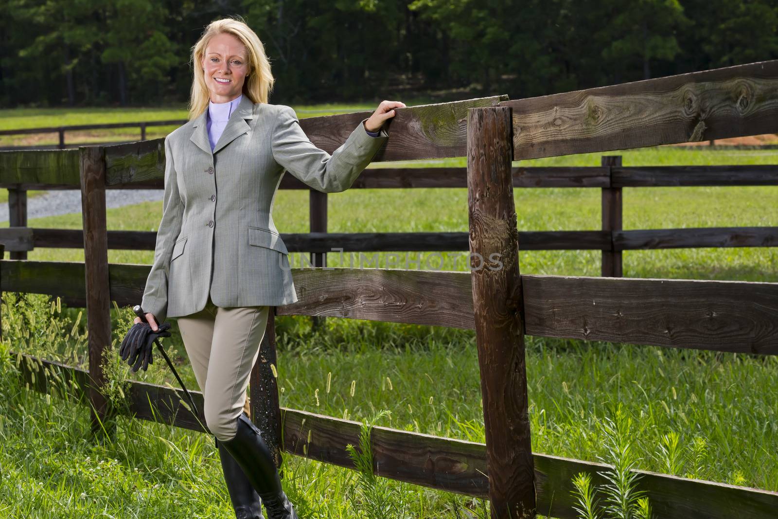 A blonde equestrian model poses outdoors before a horse show