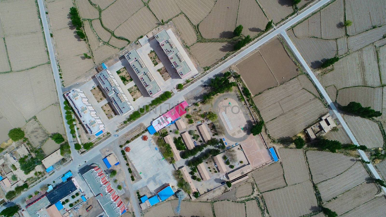 Aerial view of small poor village with school in the middle of dry farmland by Bonandbon