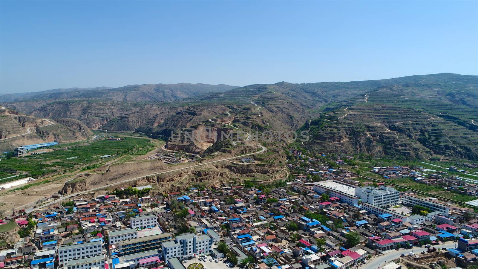 Aerial view of small poor town next the arid terraced farm firld mountain in Gansu region, China