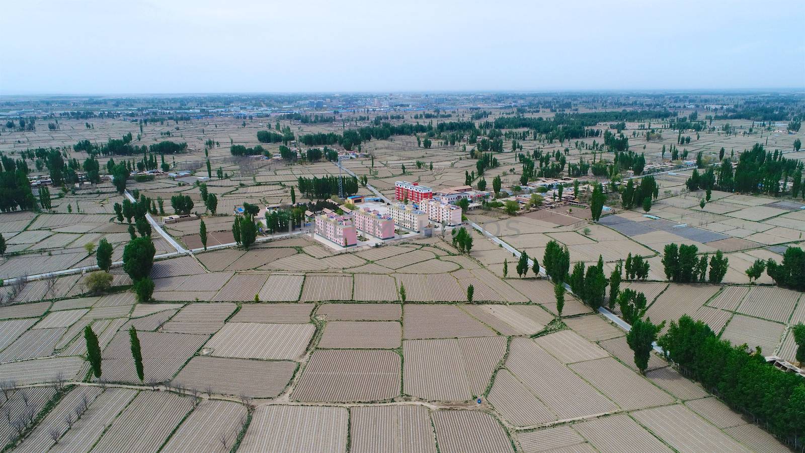 Aerial view of small poor village with school in the middle of dry farmland by Bonandbon