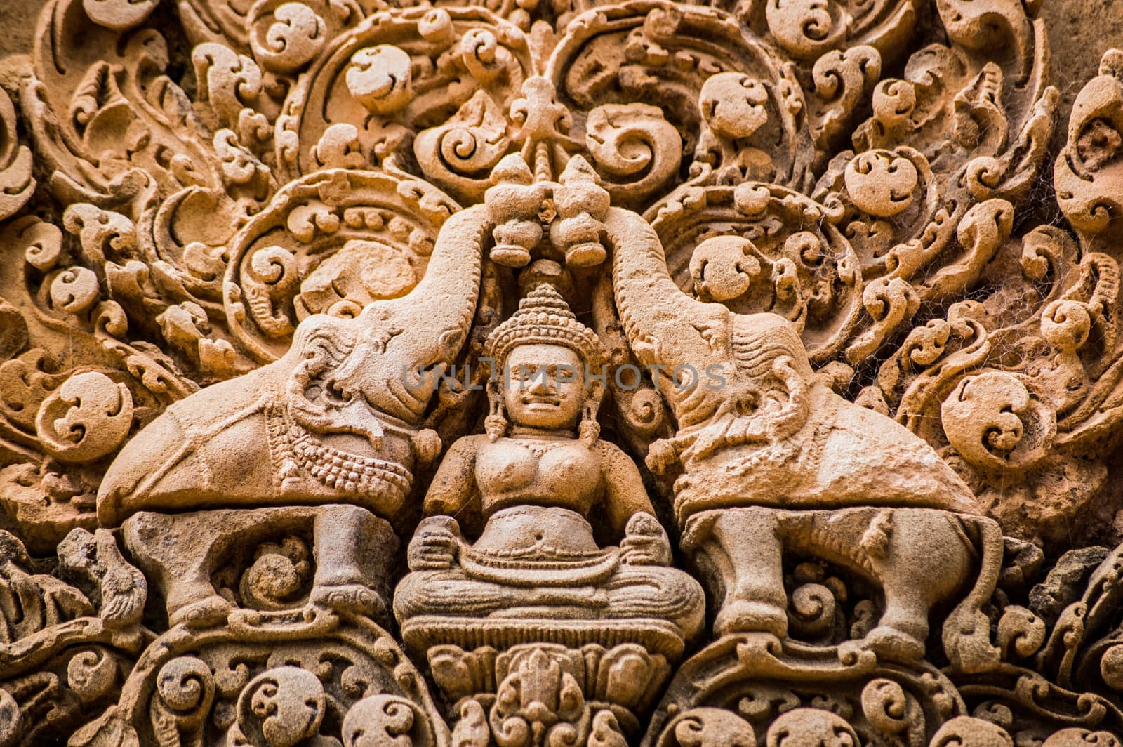 Ornate bas relief carving of the Hindu god Indra surrounded by elephants. Red sandstone lintel at the ancient Banteay Srei Temple, Angkor, Cambodia.