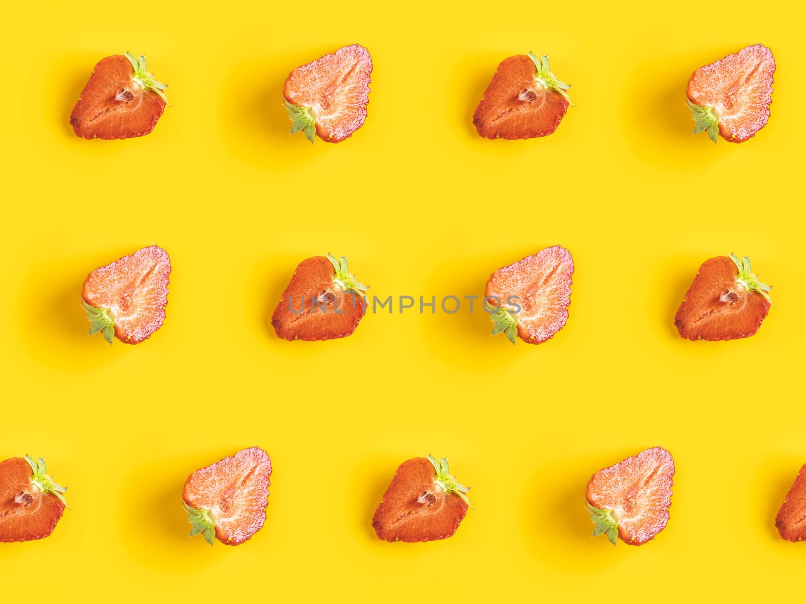Diagonal pattern from ripe juicy strawberries cut in half on bright yellow background. Creative minimalist flat lay. Vitamins vegan healthy diet concept. 