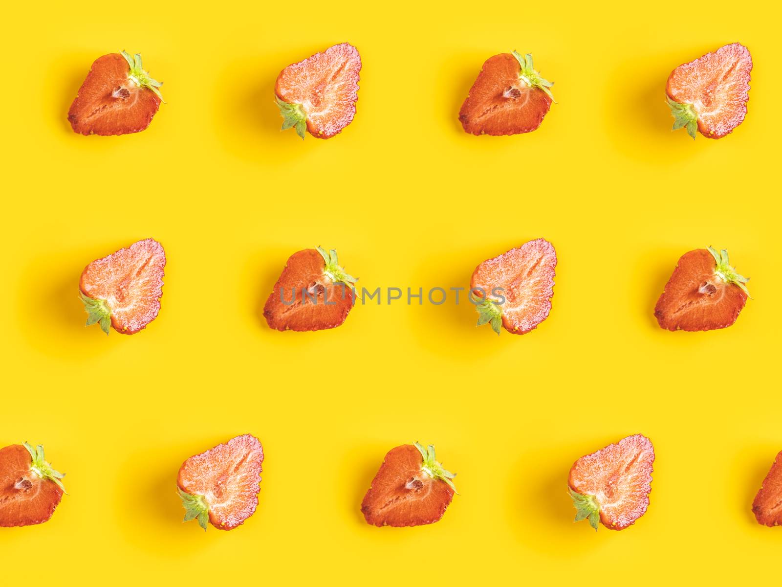 Diagonal pattern from ripe juicy strawberries cut in half on bright yellow background. Creative minimalist flat lay. Vitamins vegan healthy diet concept. 