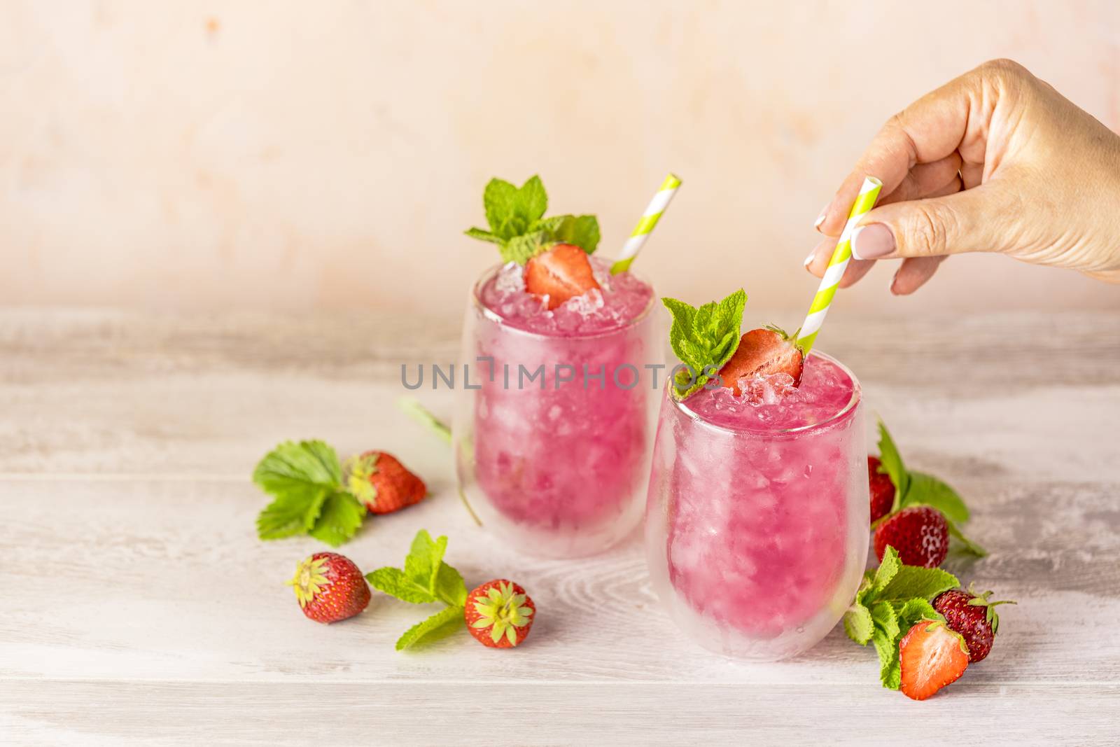 Fresh strawberry cocktail. Fresh summer cocktail with strawberry and ice cubes. Glass of strawberry soda drink on light pink background.