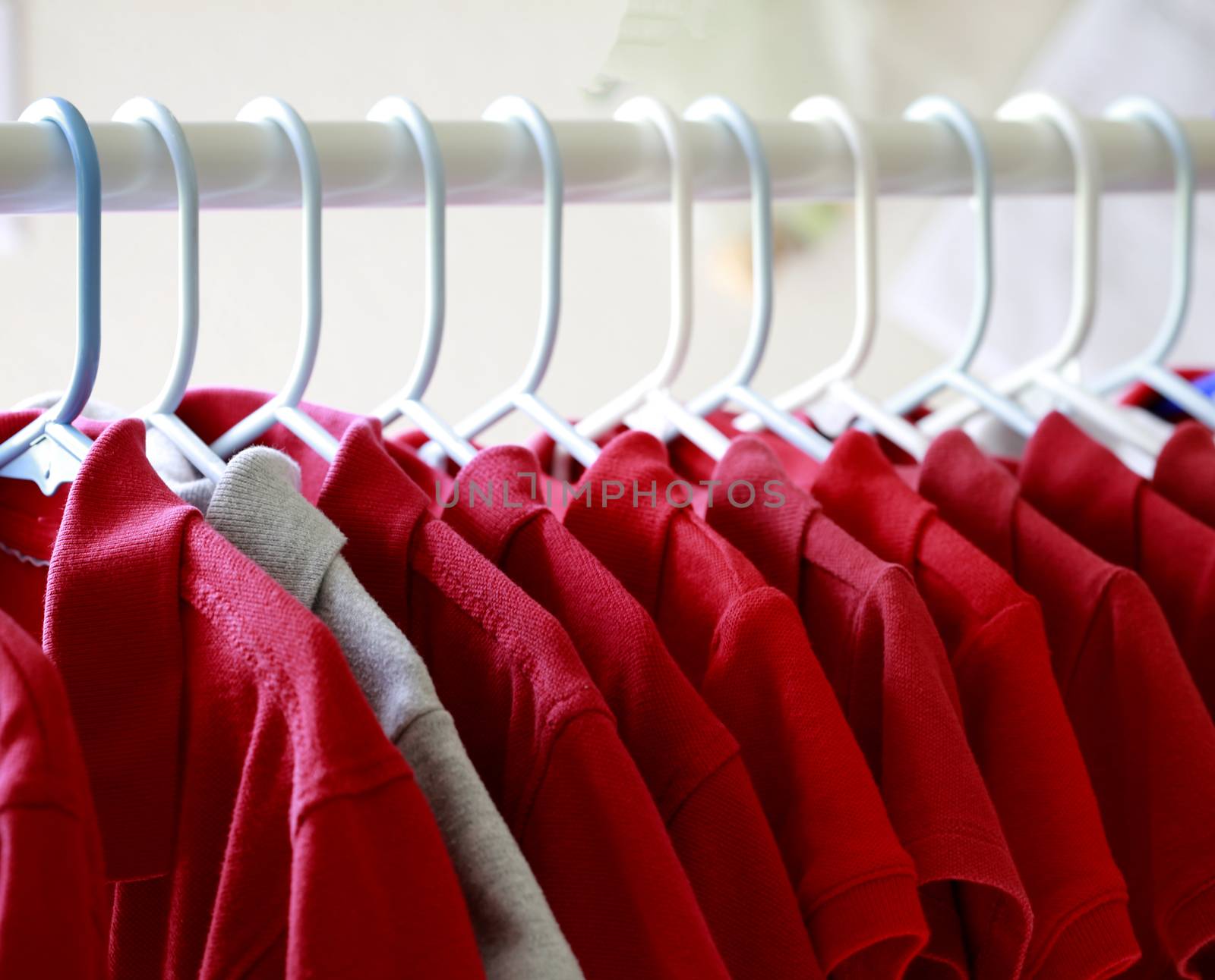 Red and one gray school uniform shirts on hangers. Selective focus.