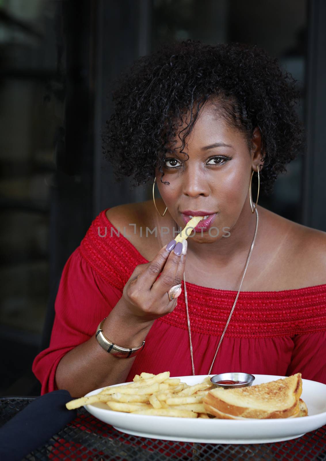 Beautiful African American woman with fancy manicure enjoying Sandwich and french fries