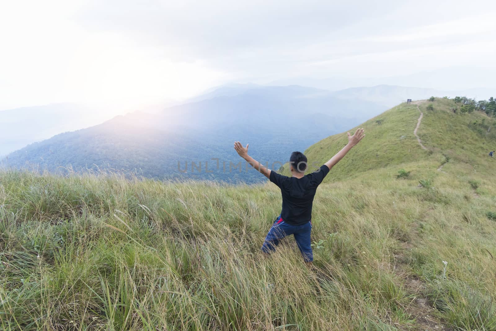 Happy young man standing with raised arms in mountains