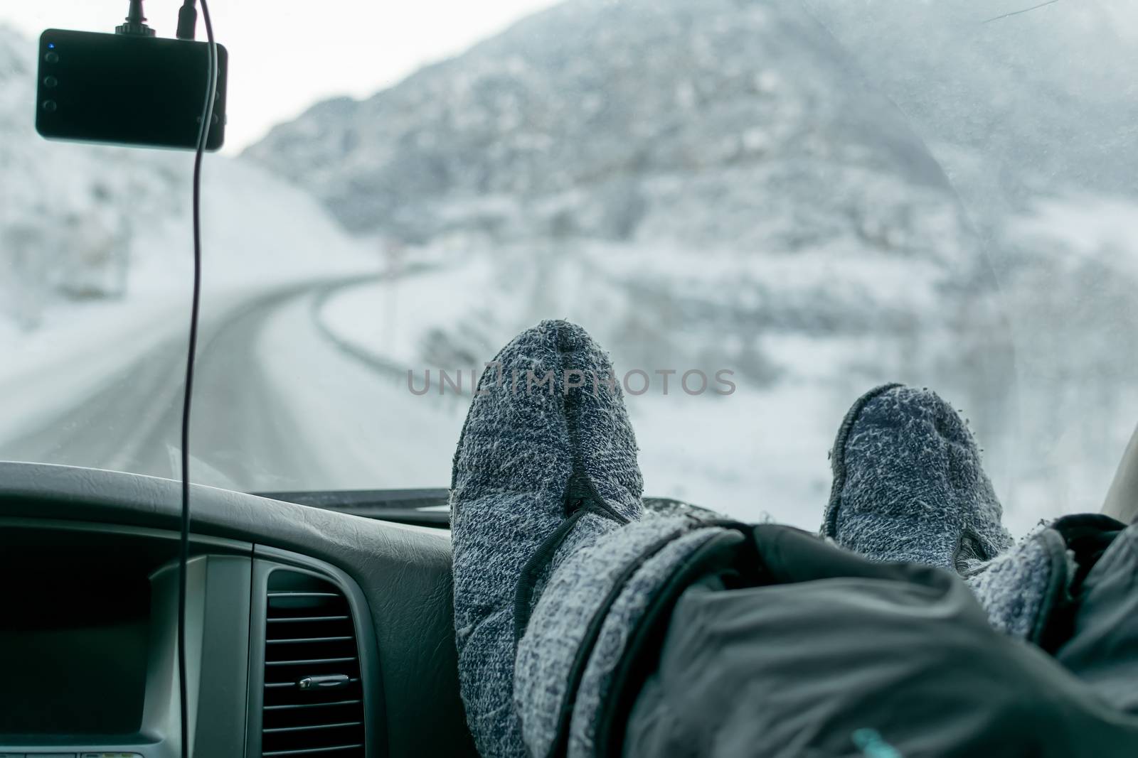 human feet in warm boots on the panel of the car, on the background of broken windshield and winter slippery snow-covered road in the highlands